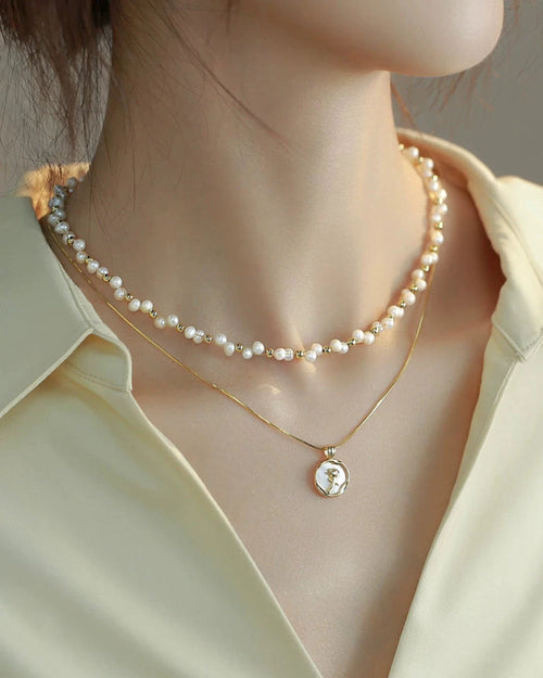 Pearl necklace and gold pendant necklace on a person wearing a light green shirt.