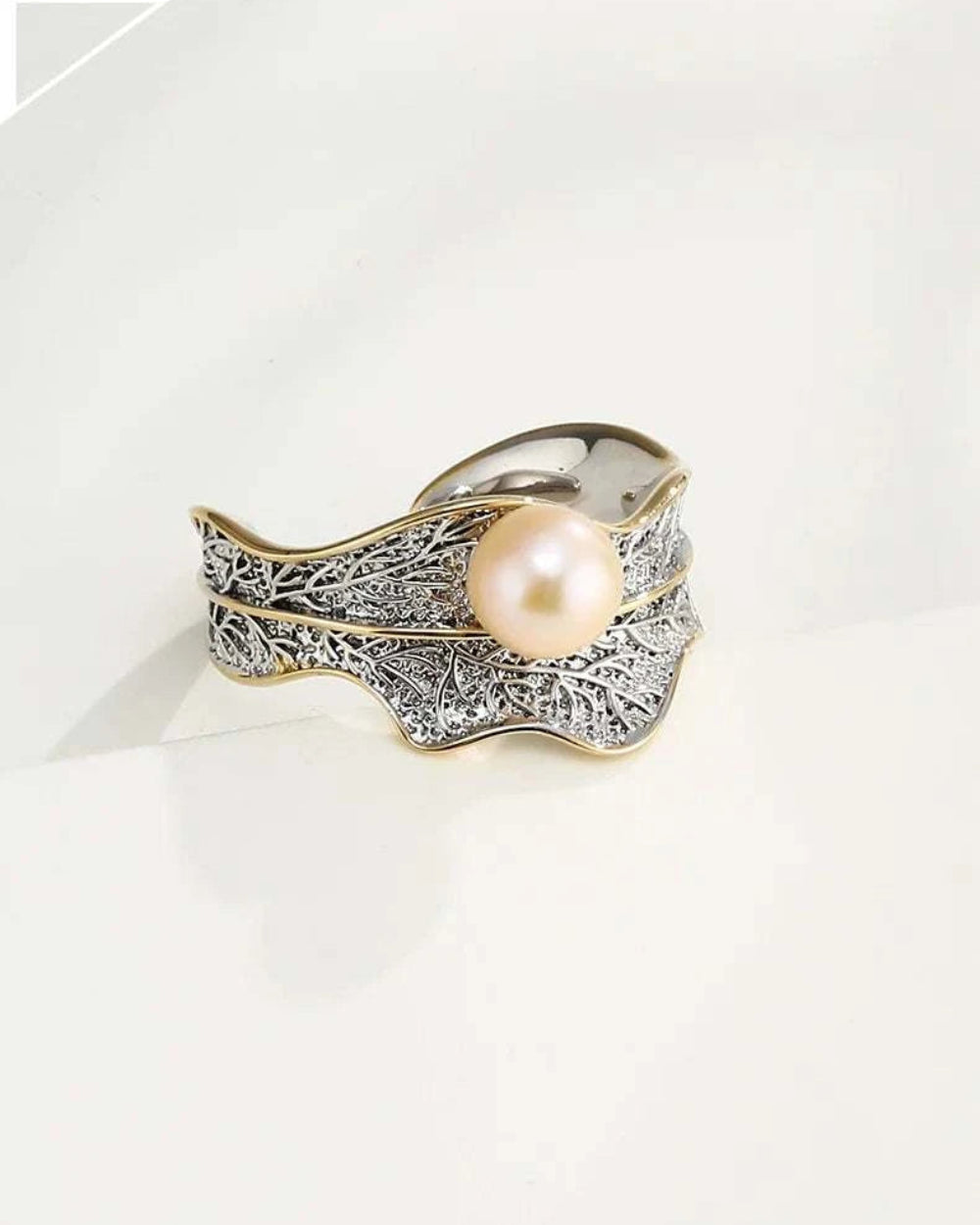 Pearl ring with intricate gold and silver design on a white background