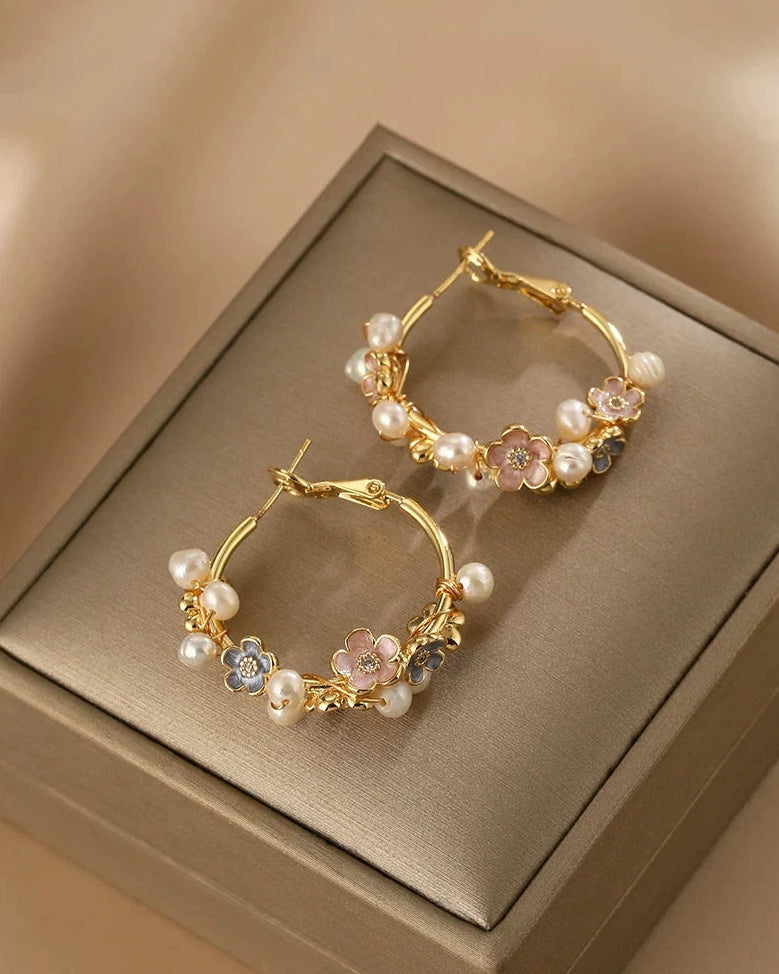 Gold hoop earrings with pearls and gemstones on a beige box