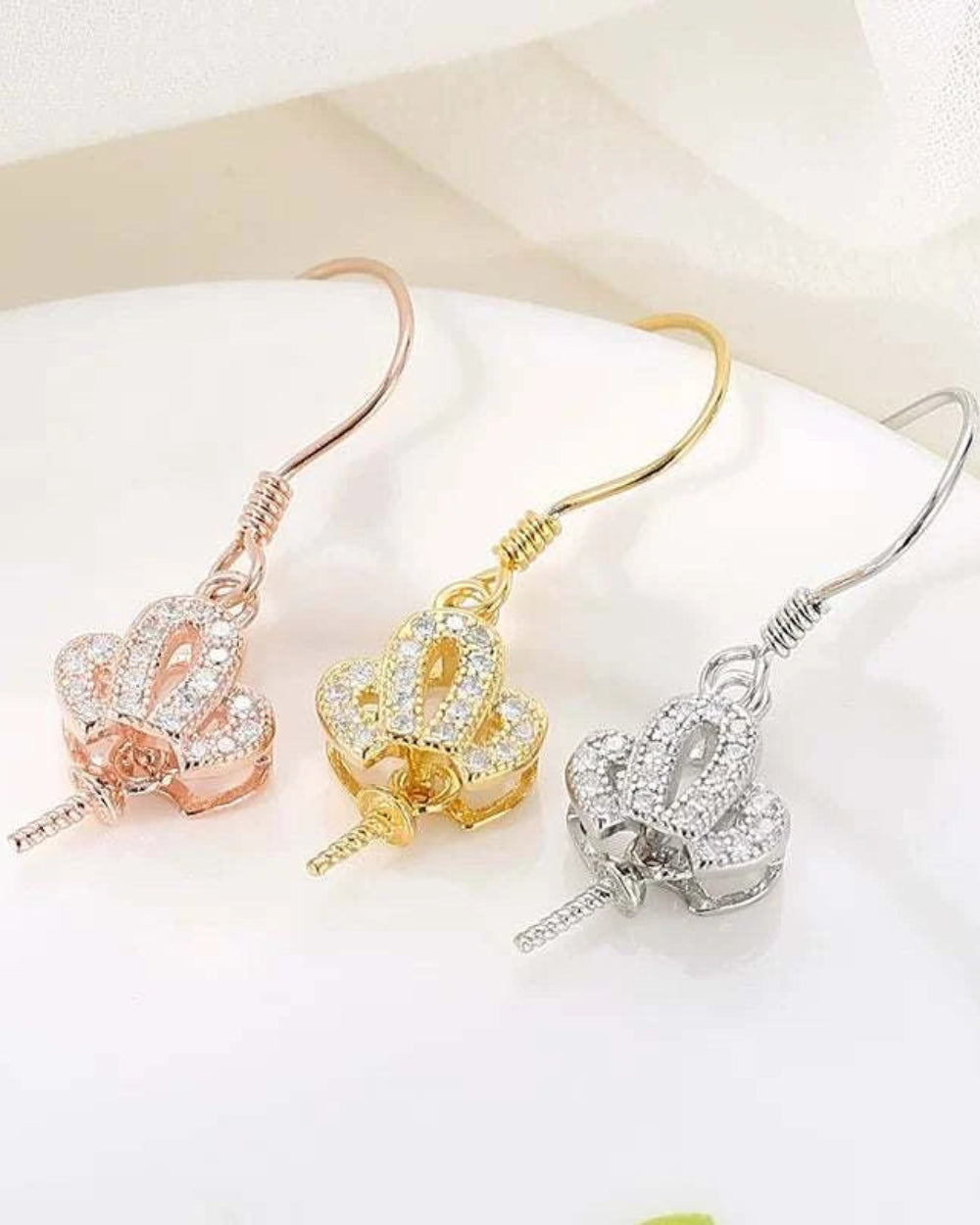 Three pairs of earrings in rose gold, gold, and silver on a white surface.