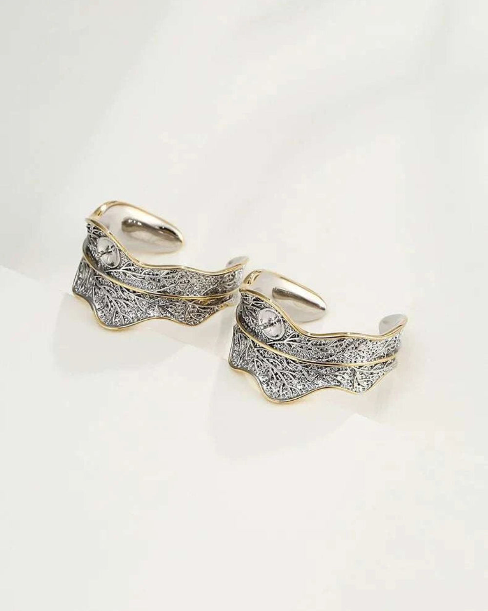 Pair of gold feather-shaped earrings on a light gray background
