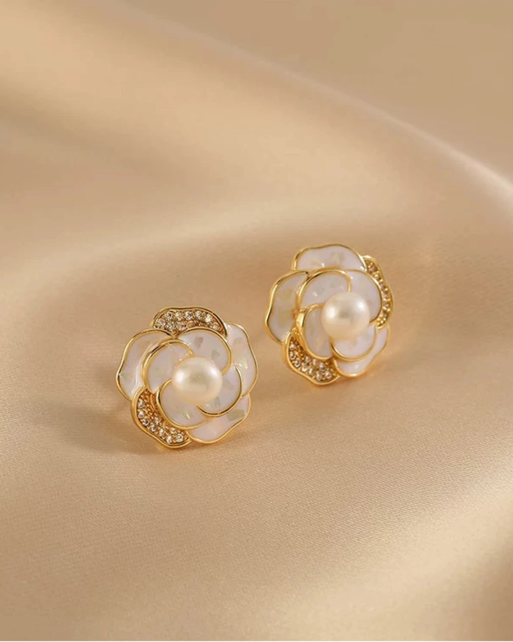 Pair of gold and pearl flower-shaped earrings on a beige fabric background