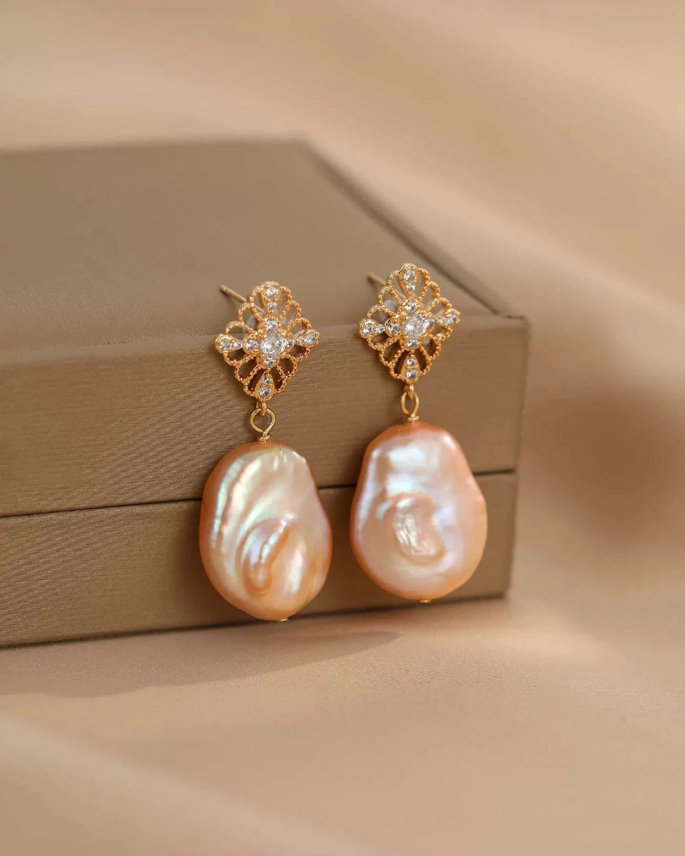 Pair of pearl earrings with gold clasps on a beige surface