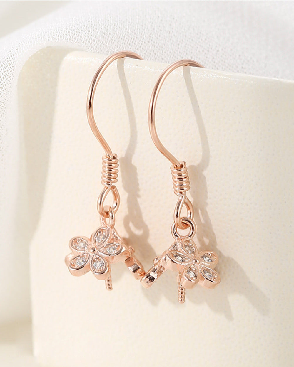 Rose gold earrings with clover designs on a light background