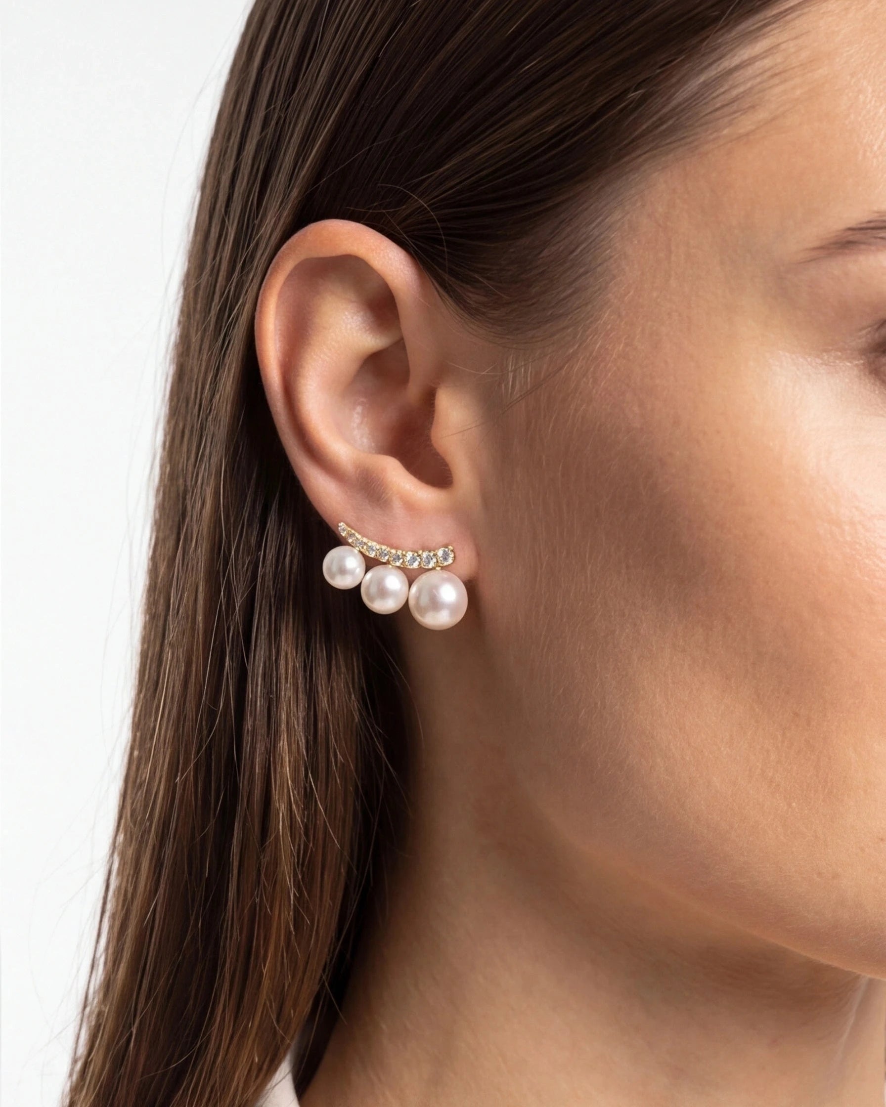 Close-up of a woman wearing pearl earrings with a plain background